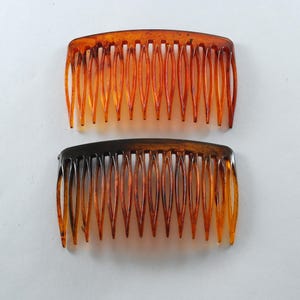 Könnte beinhalten: Zwei braune Plastikhaarkämme mit einem breiten Zahndesign. Die Kämme sind aus durchsichtigem braunen Kunststoff mit einer dunkleren braunen Tönung.