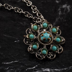 May include: A silver chain necklace with a pendant featuring a silver filigree design with turquoise blue stones.