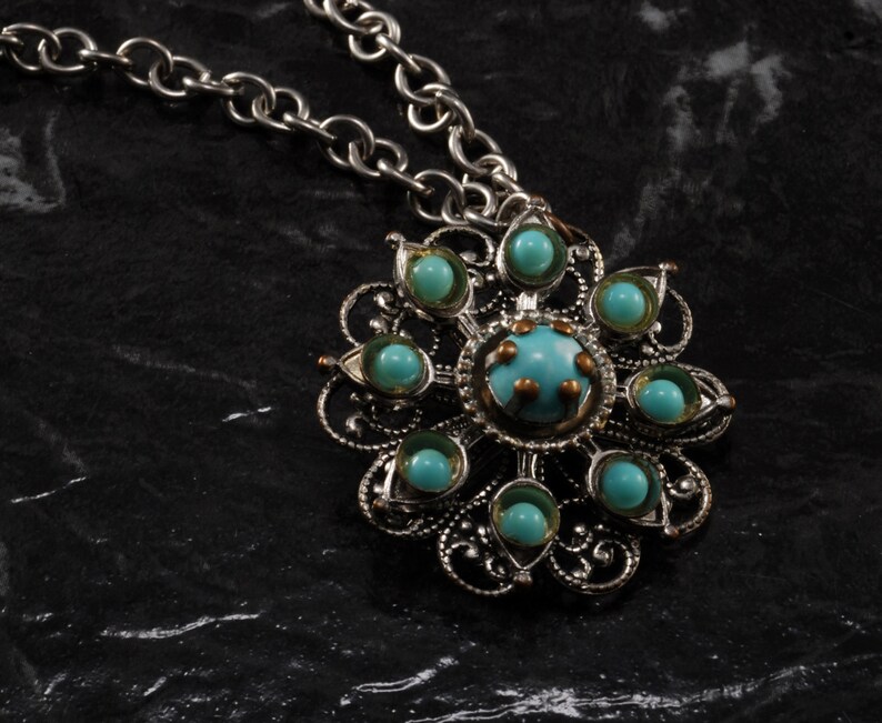 May include: A silver chain necklace with a pendant featuring a silver filigree design with turquoise blue stones.