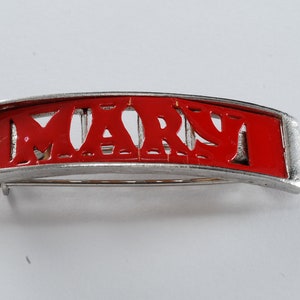 May include: A silver-toned barrette with a red enamel inlay that reads "MARY".
