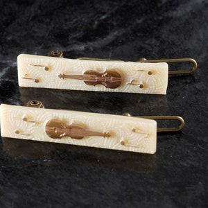 May include: Two white plastic hair clips with gold musical notes and a gold violin design.