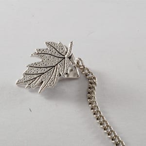 May include: Silver tone leaf charm with a chain attached. The leaf has a detailed design and is a popular accessory for jewelry making.