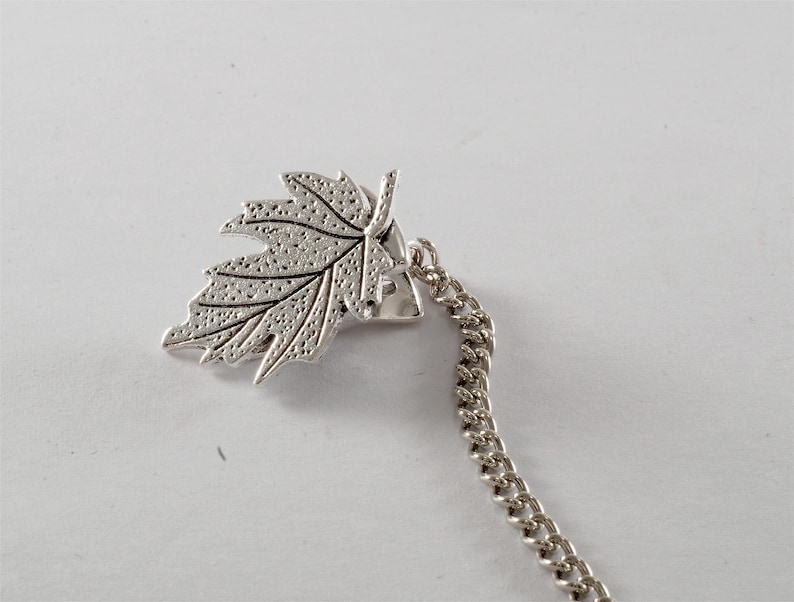 May include: Silver tone leaf charm with a chain attached. The leaf has a detailed design and is a popular accessory for jewelry making.