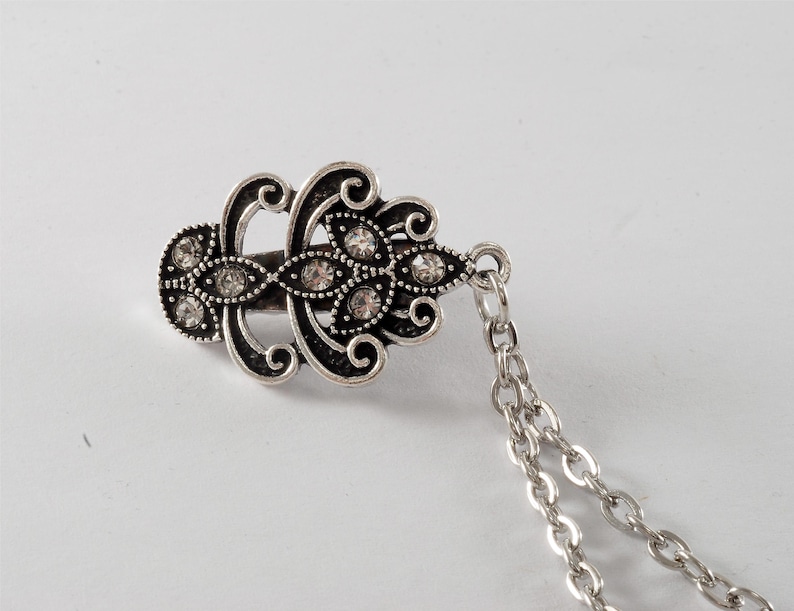 Puede incluir: Pinza para el pelo de plata con un dise&ntilde;o decorativo y brillantes transparentes. La pinza est&aacute; unida a una cadena de plata.