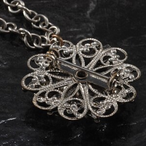 May include: Silver filigree pendant with a pin back closure. The pendant is in the shape of a flower with a delicate design.