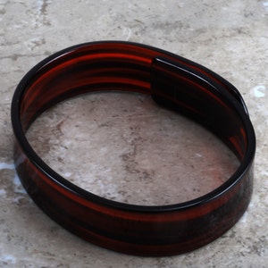 May include: A brown and black plastic hair band with a smooth, glossy finish.