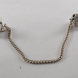 May include: A silver chain with two leaf-shaped charms. The leaves are detailed with a textured surface.