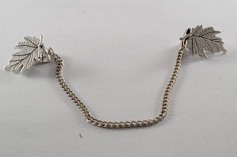 May include: A silver chain with two leaf-shaped charms. The leaves are detailed with a textured surface.