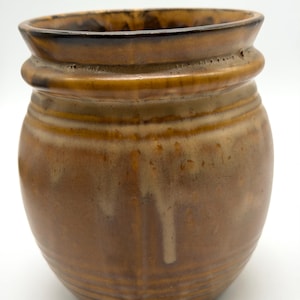 Peut inclure: Pot en céramique marron avec un corps arrondi et un bord évasé. Le pot présente des rainures horizontales et un bord marron foncé. La glaçure présente de subtiles variations de couleur.
