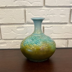 Könnte beinhalten: Eine Keramikvase mit rundem Körper und schlankem Hals. Die Vase hat einen Farbverlauf, der von Türkisblau oben zu einer grün-gelben Basis übergeht. Der Körper hat ein strukturiertes, gewebtes Muster.