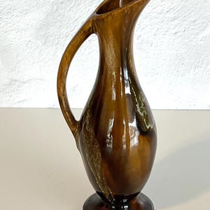 May include: A brown and white ceramic jug with a curved handle. The jug has a glossy finish and a unique swirl pattern.