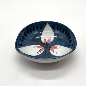 Puede incluir: Un cuenco de cerámica ovalado con un diseño único. El interior es blanco con un patrón floral azul y blanco. El borde es de color azul oscuro. Este cuenco se utiliza probablemente para servir alimentos.