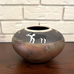 May include: A handcrafted ceramic bowl with a dark gray exterior and a black interior. The bowl features a painted black and white dog design and gold star accents. The bowl is approximately 6 inches in diameter.