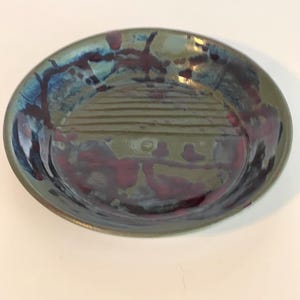Könnte beinhalten: Ein runder Keramikteller mit grüner Glasur und einem abstrakten Design in Blau und Rot.