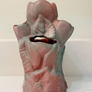 May include: A ceramic vase shaped like a rose, in pink and green hues. The vase has a textured finish and a distinctive design, suitable for home decor. The vase is approximately 20 cm tall.