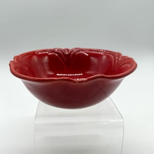 May include: A glossy red ceramic bowl featuring a scalloped rim with raised, curved detailing along the edge. The bowl has a smooth, reflective finish and a deep, rounded basin, showcasing a consistent vibrant red color throughout the entire piece.