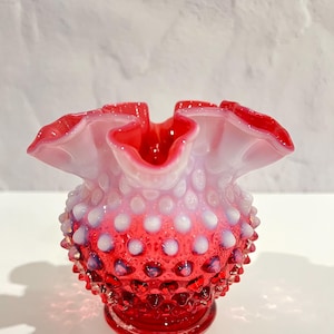May include: A small, red and white milk glass vase with a ruffled top and a textured, dotted surface.