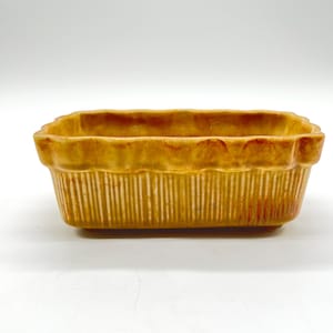 Puede incluir: Una fuente rectangular de cerámica para hornear, con exterior acanalado y borde festoneado. La fuente es de un color amarillo dorado cálido con sutiles variaciones y un aspecto ligeramente envejecido. Diseñada para hornear y servir.