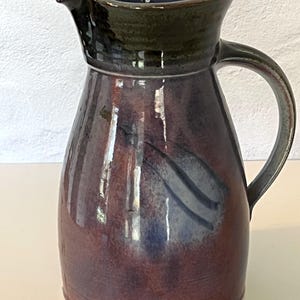May include: A ceramic pitcher with a dark purple and blue glaze. The pitcher has a wide mouth and a handle.