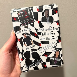 Puede incluir: Una funda de teléfono a cuadros blanco y negro con estrellas rojas y varias pegatinas. Las pegatinas incluyen una silueta de una pareja, un personaje de la saga Crepúsculo y una cita del libro. El texto en la funda dice "Team Charlie", "What if I'm the bad guy?", "And so the lion fell in love with the lamb", "You better hold on tight Spider Monkey", "Bella!" y "Where the hell have you been loca?"