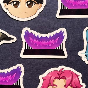 Könnte beinhalten: Eine Sammlung von Aufklebern mit Illustrationen von Charakteren im Anime-Stil. Die Aufkleber zeigen verschiedene Charaktere mit detaillierten Gesichtszügen und stilisierten Haaren. Einige Aufkleber haben ein lila Flammenmuster.