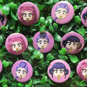 Könnte beinhalten: Eine Sammlung von rosa runden Knöpfen mit Anime-Illustrationen von Frauen, die Nudeln essen. Jeder Knopf hat eine andere Frisur und Haarfarbe, mit Nudeln, die aus ihren Mündern hängen. Die Knöpfe sind auf einem Bett aus grünen Blättern angeordnet.