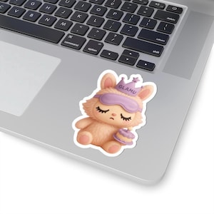 May include: A sticker featuring a sleepy cartoon bunny wearing a purple sleep mask and a crown with the word "GLAMU". The bunny is holding a small cake. The sticker is on a laptop.