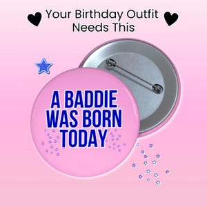 May include: A pink button with the text "A BADDIE WAS BORN TODAY" in blue. The button has a silver pin back and is surrounded by small blue stars. The text "Your Birthday Outfit Needs This" is at the top.