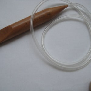 K&ouml;nnte beinhalten: Ein H&auml;kelnadel aus Holz mit einer durchsichtigen Schnur aus Kunststoff. Die Nadel ist 2,5 mm gro&szlig; und hat eine braune Farbe.