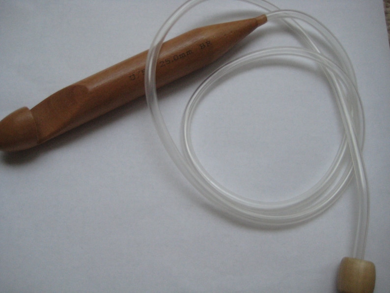 K&ouml;nnte beinhalten: Ein H&auml;kelnadel aus Holz mit einer durchsichtigen Schnur aus Kunststoff. Die Nadel ist 2,5 mm gro&szlig; und hat eine braune Farbe.