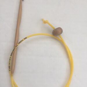 K&ouml;nnte beinhalten: Ein gelber H&auml;kelhaken mit einem Holzgriff und einer gelben Schnur mit einer Holzperle. Der Haken ist mit "SIZE 11/0 (3.75 MM)  MADE IN CHINA  DMC  T11801" beschriftet.