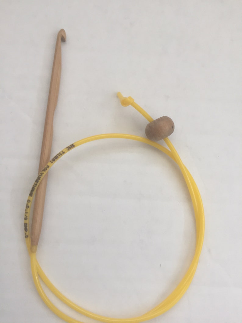 K&ouml;nnte beinhalten: Ein gelber H&auml;kelhaken mit einem Holzgriff und einer gelben Schnur mit einer Holzperle. Der Haken ist mit "SIZE 11/0 (3.75 MM)  MADE IN CHINA  DMC  T11801" beschriftet.