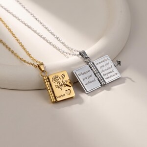 Peut inclure: Un collier doré avec un pendentif en forme de livre gravé d'une rose et du nom Scarlett, et un collier argenté avec un pendentif livre ouvert gravé du texte : Whenever you feel unloved, remember, you are cherished beyond measure.