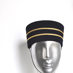 May include: A navy blue hat with two gold bands around the crown. The hat is on a silver mannequin head.