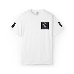 Puede incluir: Camiseta blanca con cuello redondo y mangas cortas. Un parche cuadrado negro en el pecho presenta un diseño blanco y azul. Parches rectangulares negros están en las mangas. La camiseta está hecha de un material suave.