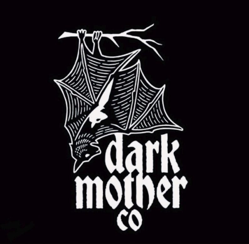 Puede incluir: Gr&aacute;fico en blanco y negro de un murci&eacute;lago colgado boca abajo de una rama. El murci&eacute;lago tiene patrones de alas detallados y est&aacute; posicionado encima de las palabras "dark mother co" en una fuente estilizada. El dise&ntilde;o est&aacute; sobre un fondo negro.