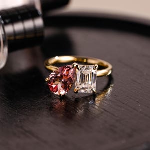 Può includere: Un anello d'oro con due pietre preziose. Una pietra è rosa a forma di pera, l'altra è una pietra trasparente rettangolare.