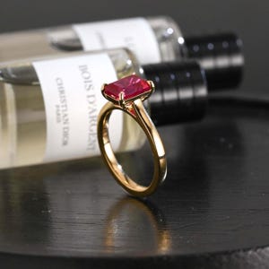 Könnte beinhalten: Ein Goldring mit einem rechteckigen, facettierten, leuchtend roten Edelstein in einer Vier-Krappen-Fassung. Die Ringschiene ist glatt und poliert und zeigt ein klassisches Design, das die tiefe karmesinrote Farbe des Steins betont.
