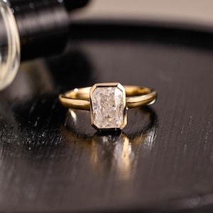 May include: A gold ring with a square-shaped diamond set in a bezel setting.