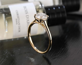 Può includere: Un anello in oro con una singola pietra preziosa trasparente a taglio brillante rotondo, fissata con una montatura a quattro griffe. La fascia è liscia e lucida, caratterizzata da un classico design solitario con finitura metallica.