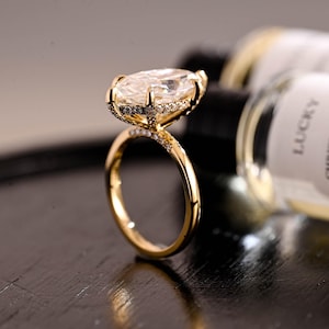 May include: A gold ring featuring a large marquise-cut center stone held by multiple prongs. The band and the basket setting are adorned with small pavé-set stones, creating a sparkling effect along the metal surface of the ring.