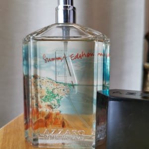 Pu&ograve; includere: Una bottiglia di profumo Azzaro Pour Homme Summer Edition in vetro trasparente con un vaporizzatore argentato. La bottiglia presenta una scena costiera e le parole "Summer Edition" in rosso. Un tappo nero &egrave; accanto.