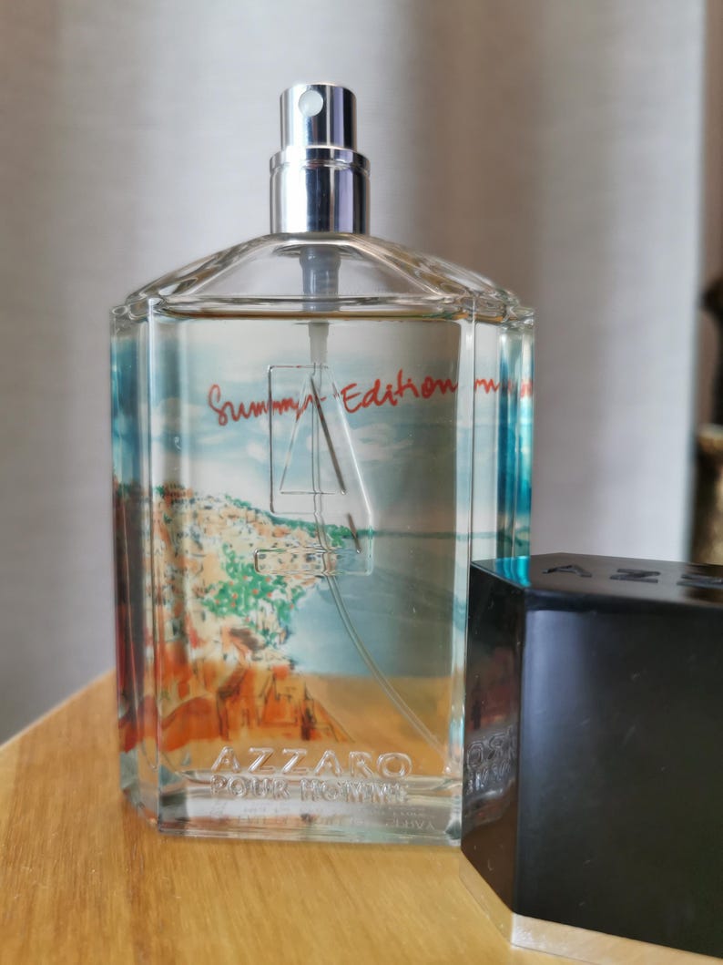 Pu&ograve; includere: Una bottiglia di profumo Azzaro Pour Homme Summer Edition in vetro trasparente con un vaporizzatore argentato. La bottiglia presenta una scena costiera e le parole "Summer Edition" in rosso. Un tappo nero &egrave; accanto.