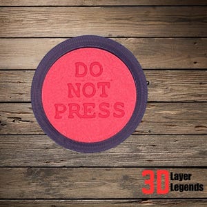 Può includere: Un pulsante circolare rosso con le parole "DO NOT PRESS" in bianco, circondato da un anello viola scuro. Il pulsante è posto su uno sfondo di legno. Il logo "3D Layer Legends" è in basso.