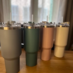 Op de afbeelding: Vier roestvrijstalen bekers met deksels en rietjes. De bekers zijn in verschillende kleuren: grijs, groen, roze en beige.
