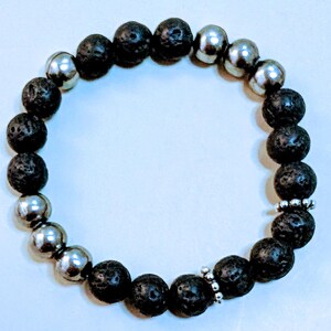 May include: A beaded bracelet featuring alternating black lava rock and silver-colored metal beads. The bracelet is strung on an elastic band, creating a flexible and comfortable fit. The beads are round and smooth, with a mix of matte and shiny finishes.