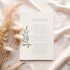 May include: A white card with the text "PSALM 23" and a German poem. The card is decorated with a watercolor olive branch and is set against a neutral background with dried flowers.