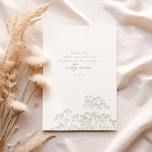 May include: A white card with the text "BEFIEHL DEM HERRN DEINE WEGE UND VERTRAUE AUF IHN. ER WIRD ES richtig machen. PSALM 37.5" in black script. The card features a delicate floral design at the bottom and is set against a soft, neutral background with dried flowers.