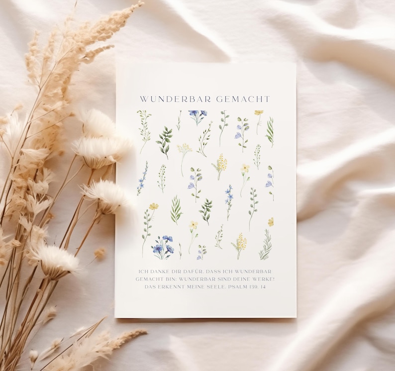 May include: A white card with the text "WUNDERBAR GEMACHT" and a floral design. The card features watercolor illustrations of various flowers in shades of green, yellow, and blue. The bottom of the card has additional text in German.