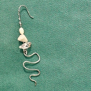Pode incluir: Um único brinco prateado com um gancho, apresentando um design em espiral e adornado com três pedras de cor clara. O brinco está sobre um fundo verde texturizado.